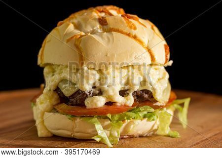 Close Up Of A Homemade Burger With Extra Cheese On A Chopping Wood Board, On Black Background