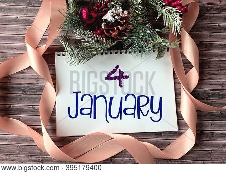 January 4 On A White Notepad.nearby Fir Branches, Red Berries, Cones And A Ribbon On A Wooden Backgr