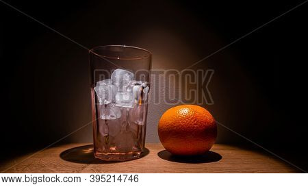 Bright Orange And A Glass With Ice On A Wooden Table.