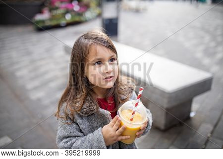 Adorable Little Girl In The Street Holding A Yellow Smoothie
