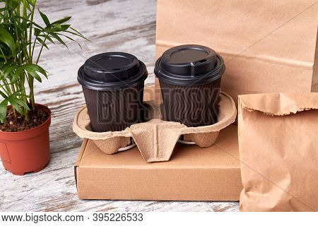 Two Closed Paper Cups Of Coffee In Cupholder. Kraft Paper Packaging On The Wooden Table.