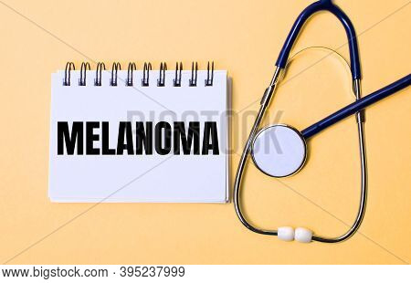 On A Beige Background, A Stethoscope And A White Notepad With The Inscription Melanoma. Medical Conc