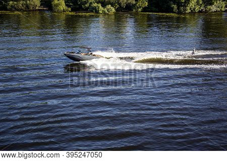 Speedboat Towing An Athlete On A Board Against The Background Of The Forest. Athlete Water Skiing An