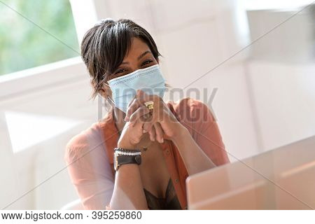 Portrait of smiling worker with surgical face mask, view through plexiglas protection