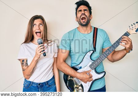 Beautiful young couple of boyfriend and girlfriend singing song using microphone and guitar angry and mad screaming frustrated and furious, shouting with anger looking up. 