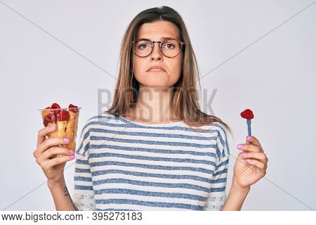 Beautiful caucasian woman eating fresh and healthy fruit relaxed with serious expression on face. simple and natural looking at the camera. 