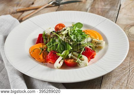 Roasted pepper salad with calamari and fresh greens. Rustic wooden table and grey textile