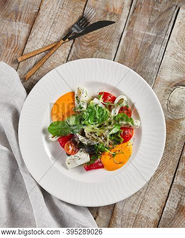 Roasted pepper salad with calamari and fresh greens. Rustic wooden table and grey textile