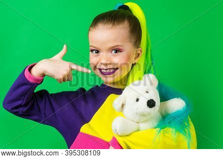 Little Model With Colored Hair Embracing And Pointing On Teddy Bear. The Concept Of Childrens Attach