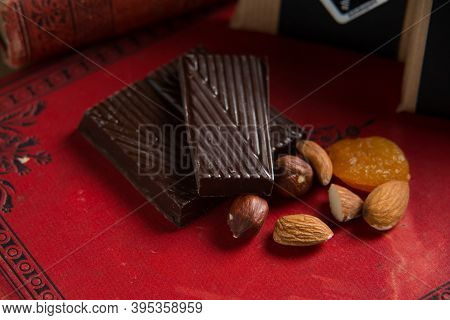 Close-up Of A Homemade Chocolate Bar With Raisins, Dried Apricot And Nuts On Red Book Background