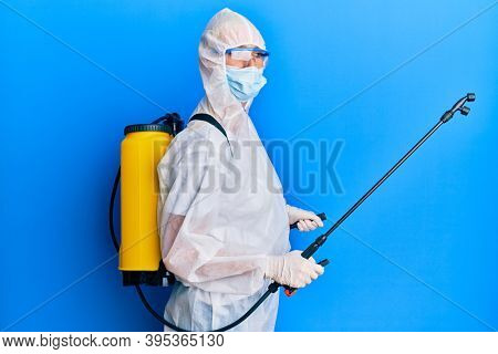 Covid specialist wearing decontamination protective suit and disinfectant spray, decontaminate and sanitize surface, standing over blue background