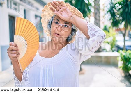 Middle age woman with grey hair using handfan on a very hot day of a heat wave