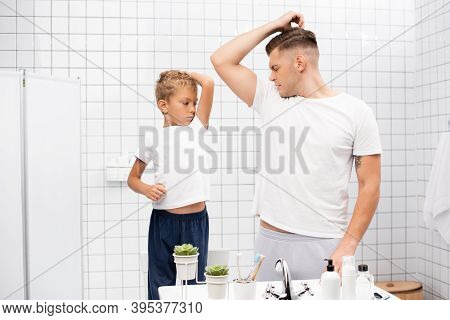 Father And Son Smelling Armpits While Standing Near Sink With Toiletries In Bathroom, Stock Image