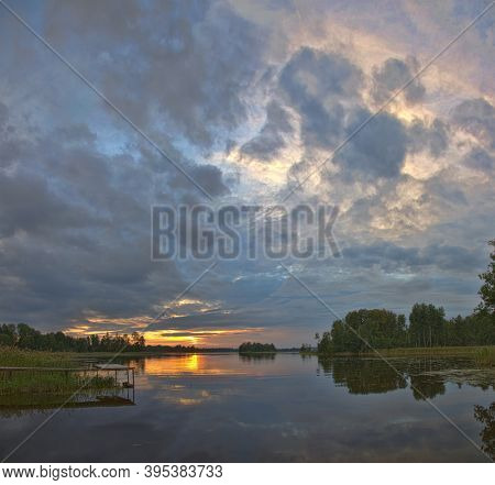 orange sunset in large clowds above river