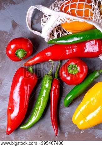 Peppers Of Different Sorts Scattering Out Of The Mesh Bag On The Grey Table