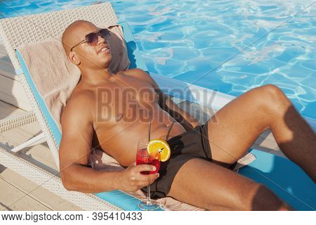 Attractive Relaxed African Man Enjoying Sunbathing, Having A Drink At The Poolside. Handsome Athleti
