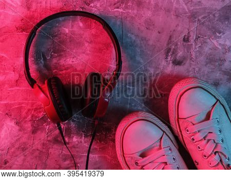 Wired Headphones And Sneakers On Concrete Background. Neon Blue-red Gradient Light. Retro Wave, 80s 
