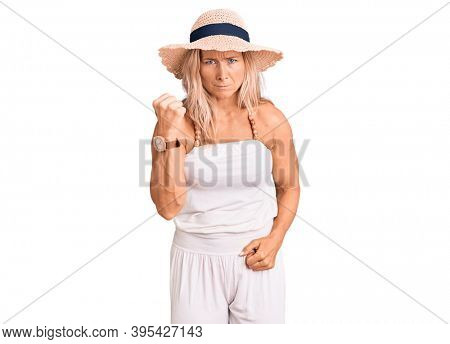 Middle age fit blonde woman wearing summer hat angry and mad raising fist frustrated and furious while shouting with anger. rage and aggressive concept. 