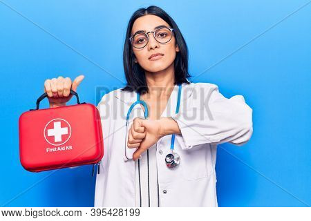 Young beautiful latin woman wearing doctor stethoscope holding first aid kit with angry face, negative sign showing dislike with thumbs down, rejection concept 