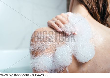 Close-up Of A Female Shoulder In Foam. The Girl Takes A Bath With Foam. Body Care, Skin Care, Aspara