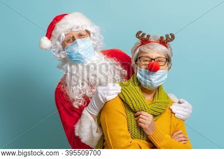 Merry Christmas and Happy Holidays! Santa Claus and reindeer on bright color background. Senior people in carnival costumes wearing face masks during Covid-2019