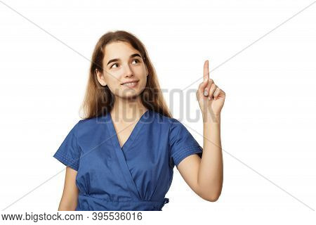 Young Beautiful Female Doctor In A Blue Surgical Gown Shows A Finger To The Side Isolated On A White