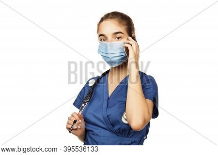 Young Beautiful Female Doctor In Blue Surgical Gown With Stethoscope Speaks On The Phone With A Pati