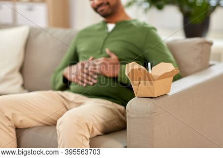 consumption and people concept - cup of takeaway food in front of overeaten man at home
