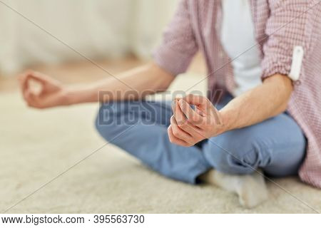 mindfulness, yoga and people concept - close up of man meditating in easy pose at home