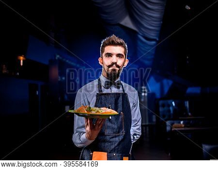 Professional Waiter Helpfully Serves Salad On A Black Background.