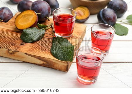 Delicious Plum Liquor And Ripe Fruits On White Wooden Table. Homemade Strong Alcoholic Beverage