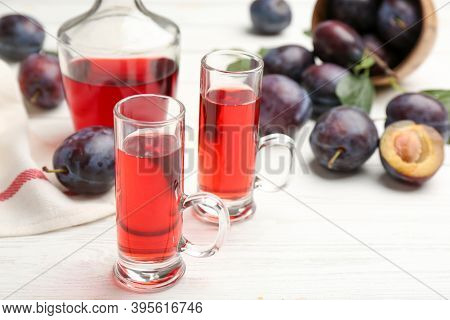 Delicious Plum Liquor And Ripe Fruits On White Wooden Table, Closeup. Homemade Strong Alcoholic Beve