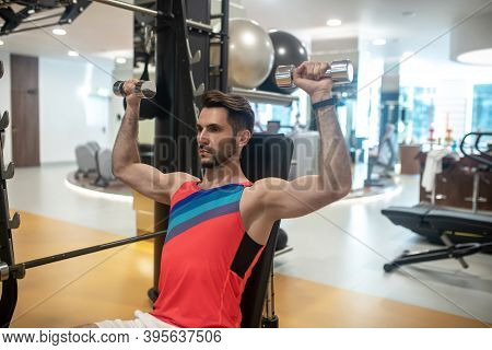 Young Dark-haired Man Working On His Arms On A Gym Machine And Looking Concentrated