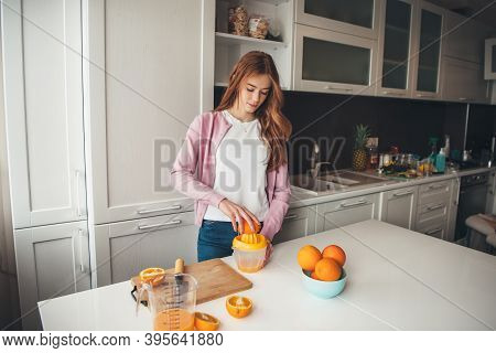 Caucasian Ginger Woman With Freckles Is Manually Squeezing Orange Juice In The Kitchen
