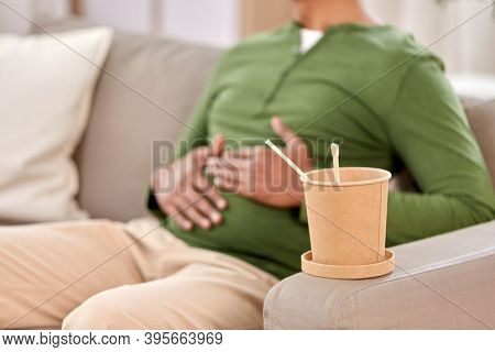 consumption and people concept - cup of takeaway food in front of overeaten man at home