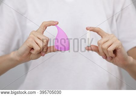 Close Up View Of Young Woman Making Choice Between Menstrual Cup And Tampon, On White Background. Gy