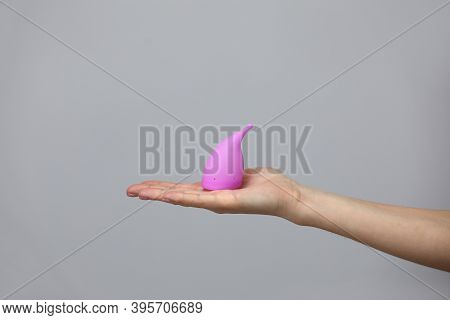 Young Woman Hand Holding A Pink Menstrual Cup - Gray Background. Gynecology Concept