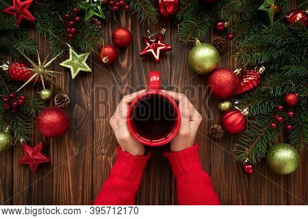 Woman Holding Hot Christmas Tea Against Decorations On Wooden Table. Top View. New Year Or Christmas