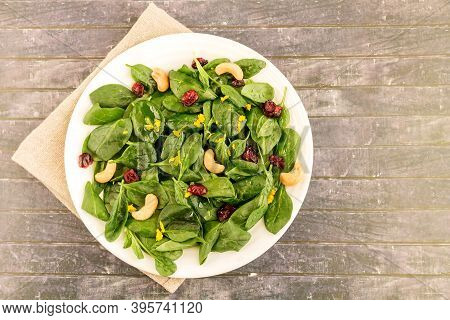 On A White Plate, Fresh Green Vitamin Salad Of Young Spinach With Dried Cranberries, Cashews, Zest A