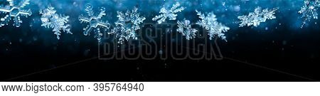Cold winter snowflakes falling with sparkling falling snow and glittering blue background.
