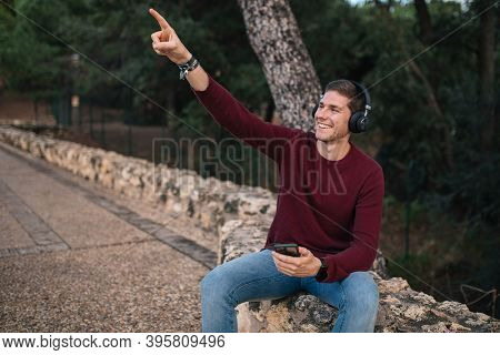 Boy Listening To Music With Wireless Headphones And Using His Cell Phone. Red Vest.