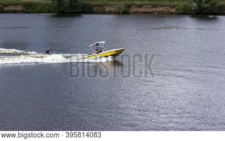 Speedboat Towing An Athlete On A Board Against The Background Of The Forest. Athlete Water Skiing An