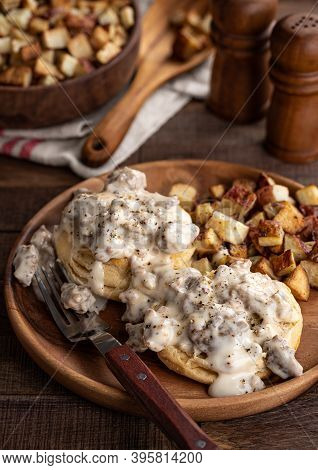 Biscuits With Creamy Sausage Gravy And Fried Potatoes On A Wooden Plate
