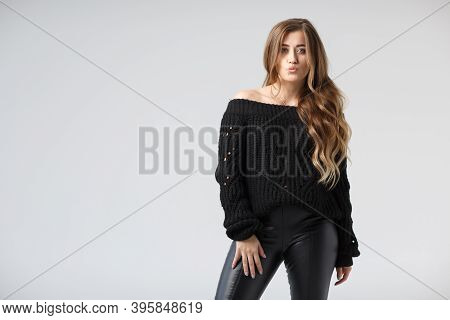 Pretty Young Woman In A Black Leather Leggings And Black Sweater Posing On A White Background. A Cau