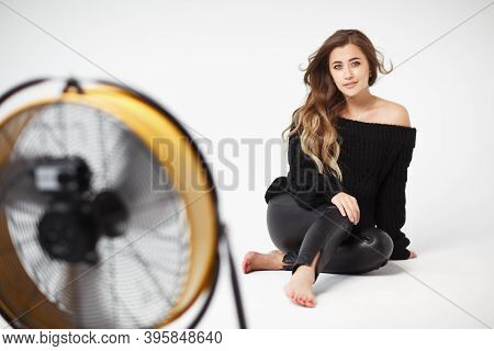 Pretty Young Woman In A Black Leather Leggings And Black Sweater Sitting On A White Background. A Ca