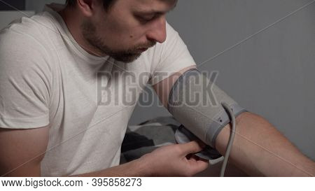 Young Man Measuring Blood Pressure At Home. Hypertensive Patient Performing An Automatic Blood Press