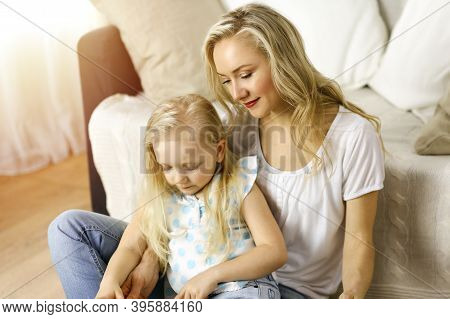 Happy Family. Blonde Young Mother Reading A Book To Her Cute Daughter While Sitting At Wooden Floor 