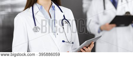 Unknown Woman Doctor Iusing Tablet Computer In Her Hands, While Standing In Clinic. Medicine Concept