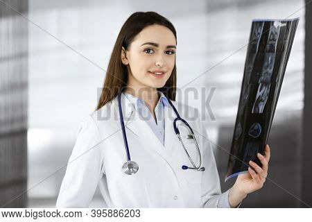 Professional Young Woman-doctor Is Looking At Her Patients Roentgenogram. Physician At Work In A Cli