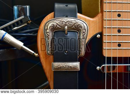 Electric Guitar And Leather Strap With Silver Buckle. Close-up With Glass Slide, Blues Harp And Cabl